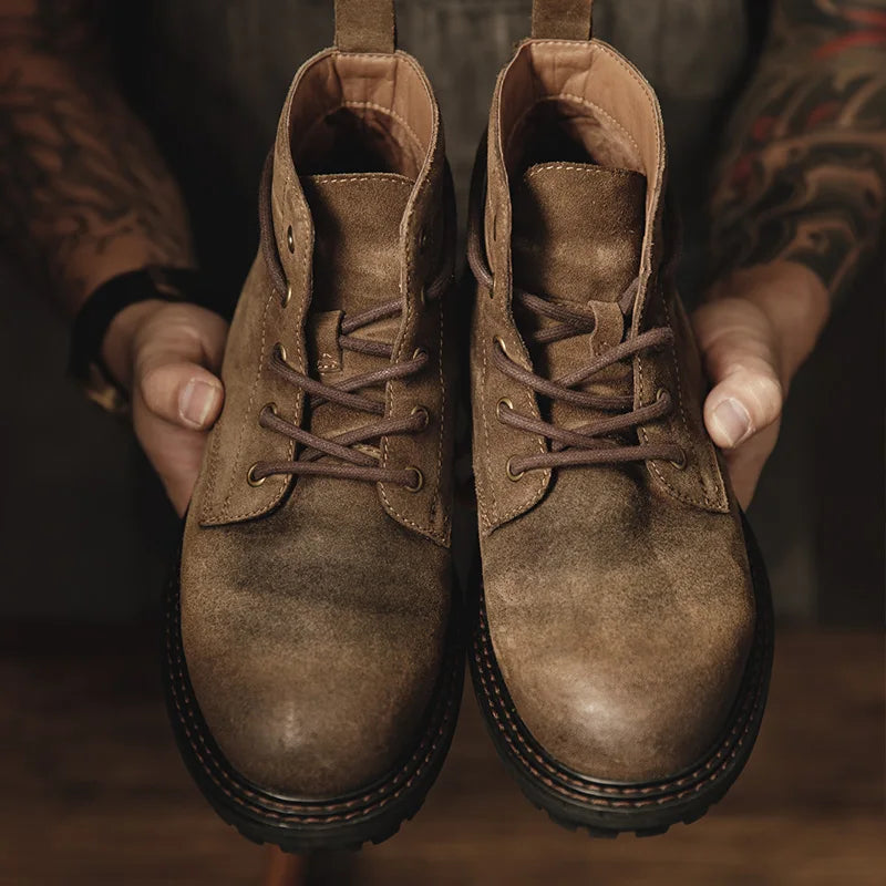 Brown leather boots held by a person with tattooed arms.