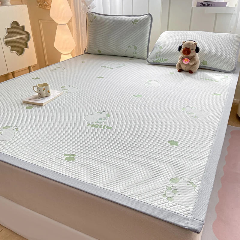 A white mesh mattress cooling pad with a light gray border and green cartoon bunny prints, shown on a bed in a bedroom setting with pillows and a small plush toy.