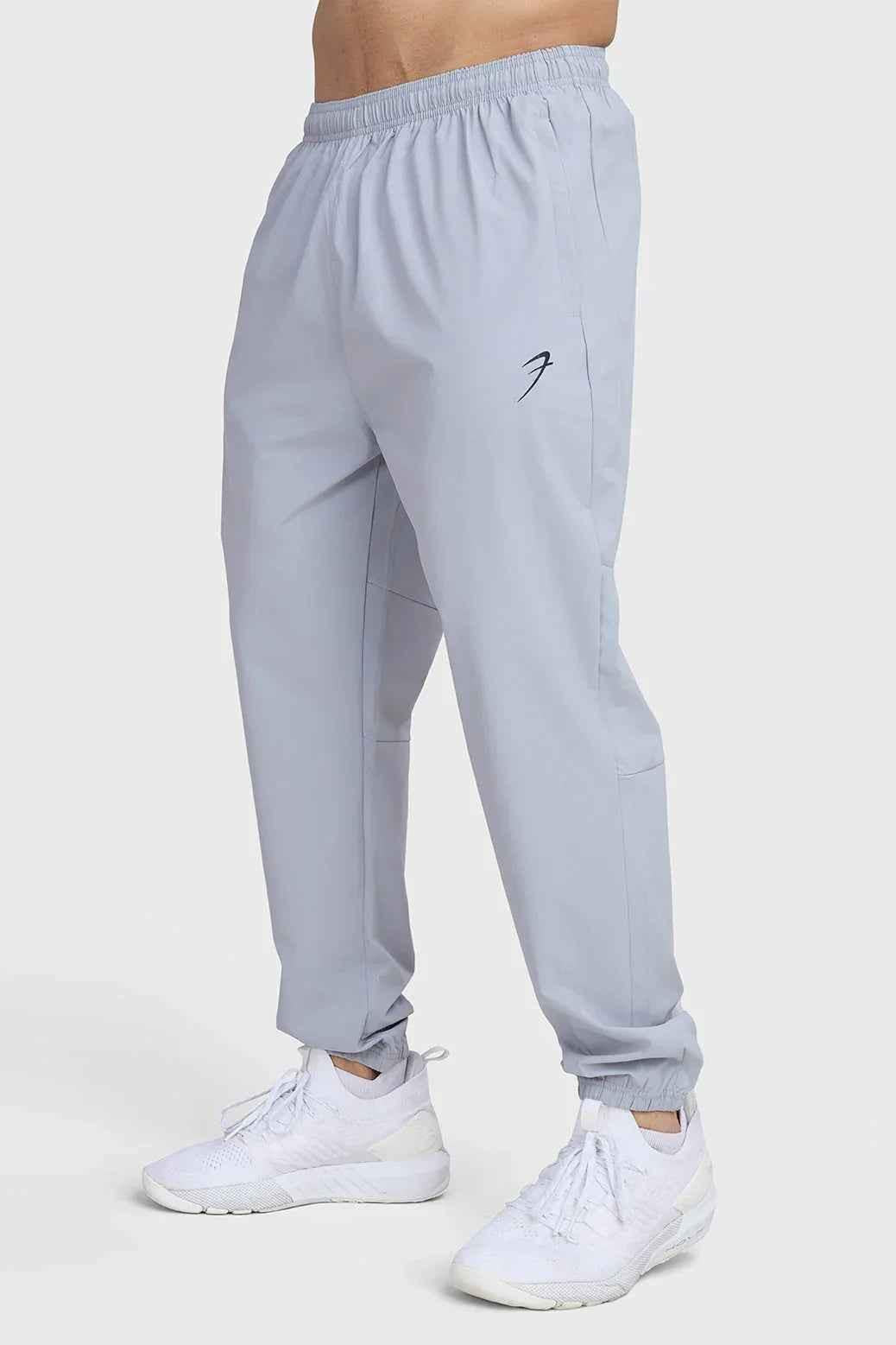 Light grey Fuaark Nz Essential Joggers track pants shown on a model, featuring a relaxed fit and elastic waistband for comfortable wear.