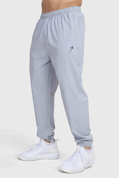 Light grey Fuaark Nz Essential Joggers track pants shown on a model, featuring a relaxed fit and elastic waistband for comfortable wear.